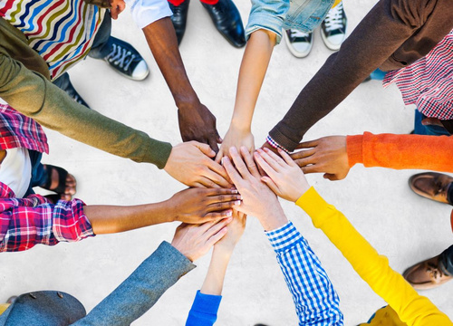 Im Kreis stehende Personen führen in der Mitte die flachen Hände zusammen. Ein Symbol für den Zusammenhalt zwischen Menschen verschiedener Herkunft.
