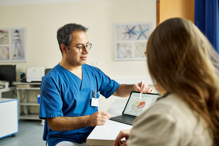 Arzt und Patientin sitzend am Tisch im gynäkologischen Informationsgespräch, zur Visualisierung wird eine Illustration auf einem Bildschirm gezeigt