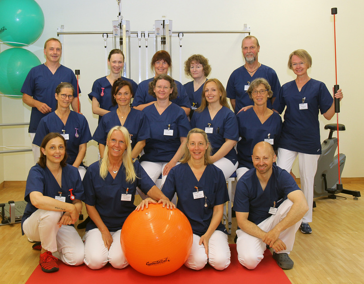 Das Team der Therapiezentrums der Klinik Husum hat sich um einen orangenen Petsyball in einem Behandlungsraum versammelt. 