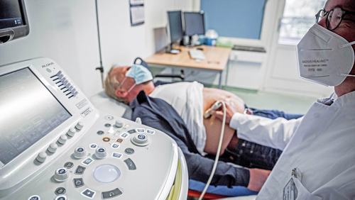 Dr. Ulf Niemann schallt den Bauch einen Patienten, der neben ihn auf einer Liege liegt. Links im Vordergrund die umfangreiche Steuereinheit des Ultraschallgerätes. 