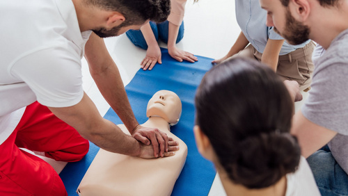 Erste-Hilfe: Rettungssanitäter führt Teilnehmer*innen die Herzdruckmassage an einer Puppe von