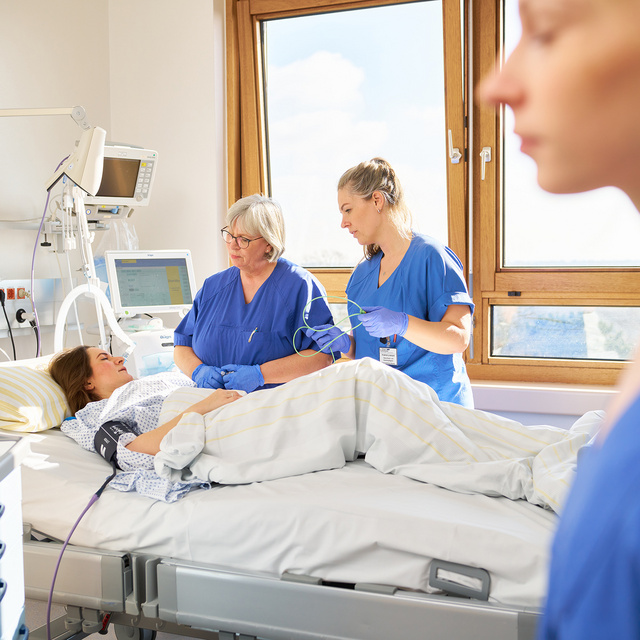Im Hintergrund des Bilder betreuen zwei Pflegekräfte eine Patientin in einem Intensivbett der Klinik Niebüll. Im Vordergrund betrachtet eine Pflegekraft einen Monitor.